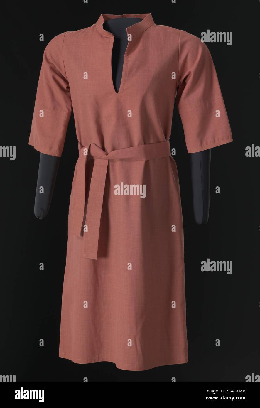 Abito in lana rosa rosa polveroso (a) e cintura corrispondente (b) progettato da Arthur McGee. L'abito A-line ha un colletto corto in piedi decorato con linee di cucitura superiore pesante in filo colorato simile, una fessura sul fronte centrale, maniche a gomito, e cade appena sotto il ginocchio. L'abito si adatta sopra la testa, non ha fissaggi. Il vestito non è foderato tranne con auto-tessuto intorno al giogo anteriore e fessura anteriore. Non sono presenti etichette. La cintura (b) è realizzata con lo stesso tessuto di lana del vestito. È decorata ad ogni estremità con le stesse linee di cucitura superiore pesante del collare dell'abito, Foto Stock