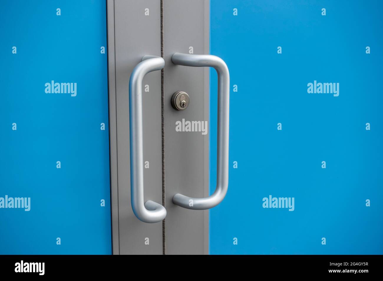 Primo piano di maniglie delle porte color argento all'esterno di un edificio d'affari, con un effetto schermo blu Foto Stock