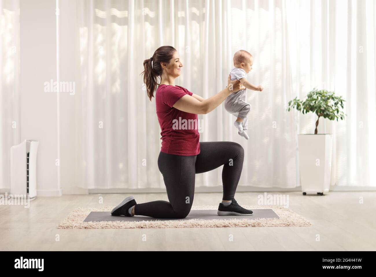 Madre che solleva un bambino e che si esercita a casa Foto Stock