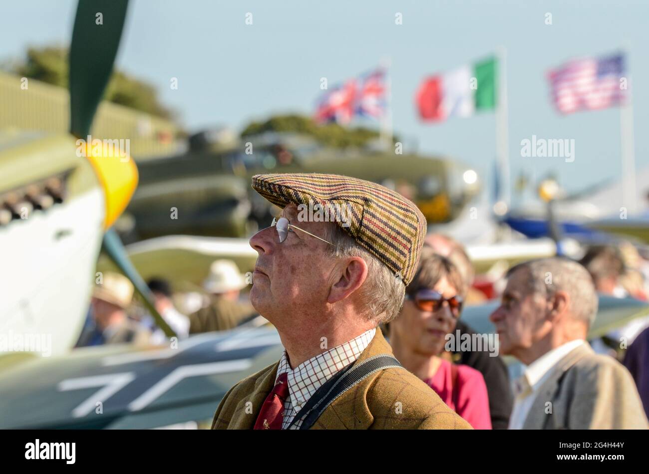 Visitatore in abbigliamento vintage guardando in su alla mostra volante all'evento vintage Goodwood Revival, West Sussex, UK. Tedesco Luftwaffe aereo. Berretto in tweed Foto Stock