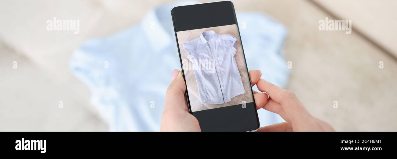 La mano femminile tiene lo smartphone e scatta foto di una camicia blu Foto Stock