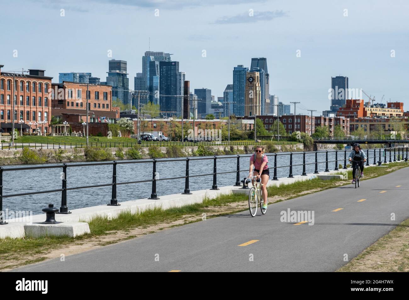 Montreal, CA - 15 maggio 2021: Donna in bicicletta sulla pista ciclabile del canale di Lachine, con skyline sullo sfondo. Foto Stock