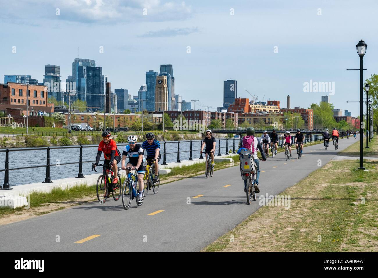 Montreal, CA - 15 maggio 2021: Persone in bicicletta sulla pista ciclabile del canale di Lachine, con skyline sullo sfondo. Foto Stock