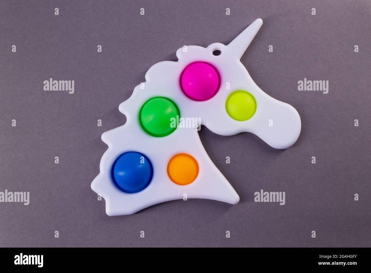 Giocattolo luminoso e colorato semplice unicorno Dimple. Popolare giocattolo anti stress su sfondo grigio Foto Stock