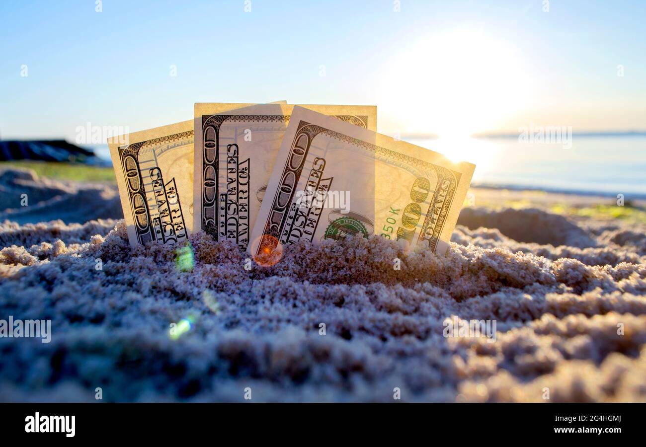 Tre dollari di bollette sono sepolti in sabbia sulla spiaggia di sabbia vicino al mare all'alba del tramonto Foto Stock