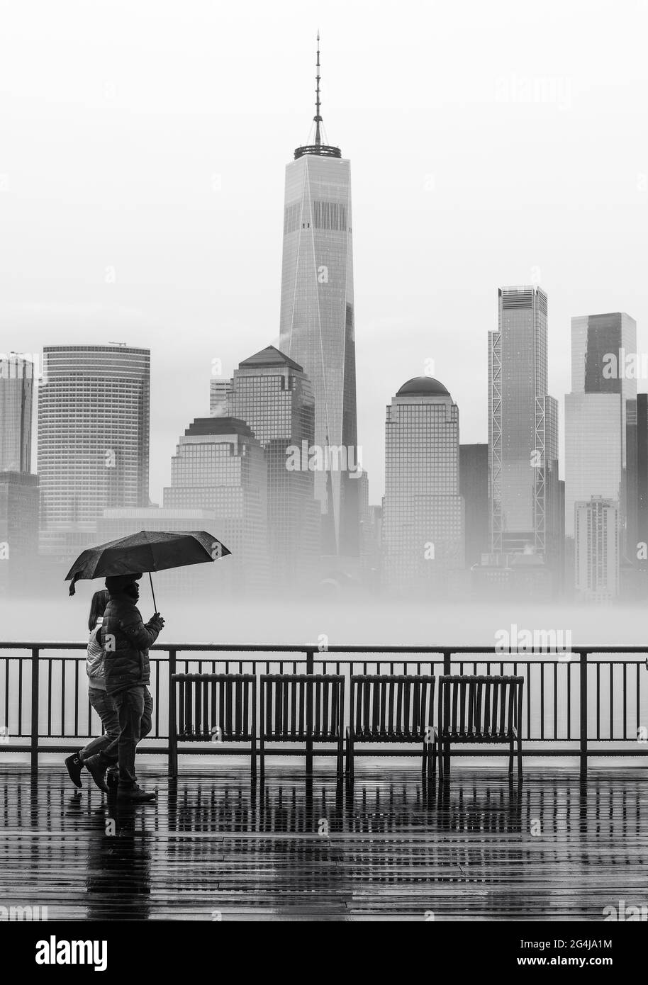 Una coppia che cammina sotto la pioggia con un ombrello in bianco e nero con lo skyline di New York sullo sfondo. Foto Stock