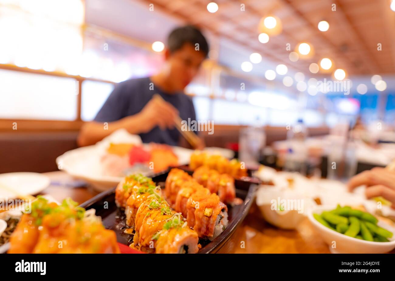 Focalizzazione selettiva sul cibo Giapponese in un ristorante Giapponese. Sushi di salmone su un piatto con l'uomo offuscato che mangia cibo giapponese con chopsticks. Foto Stock