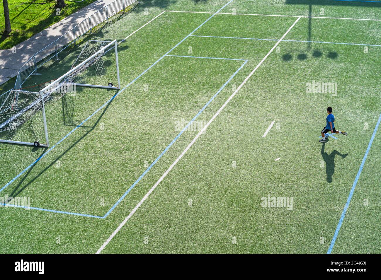 Lone uomo e la sua ombra che calcia una palla di calcio durante mezzogiorno. Foto Stock