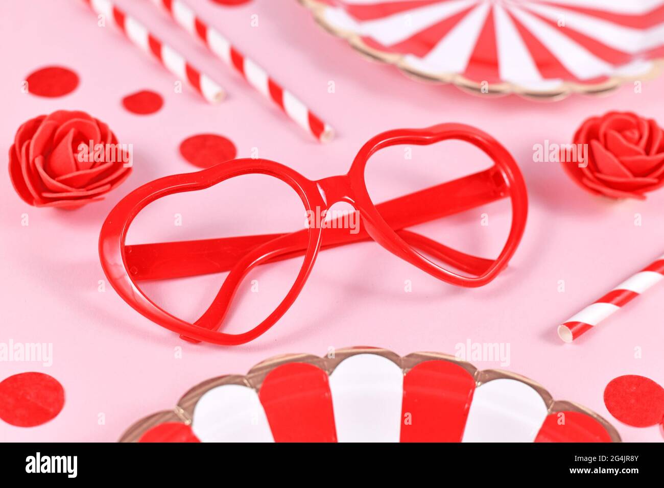 Occhiali a forma di cuore rosso, circondati da rose, confetti e piatti di  carta da festa su sfondo rosa Foto stock - Alamy