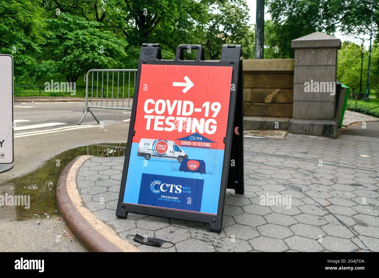 Il test di Covid-19 con una freccia indirizza i visitatori alla sede del centro di test mobile di coronavirus. Maschera facciale usata a terra. - New York, Stati Uniti d'America - 2021 Foto Stock