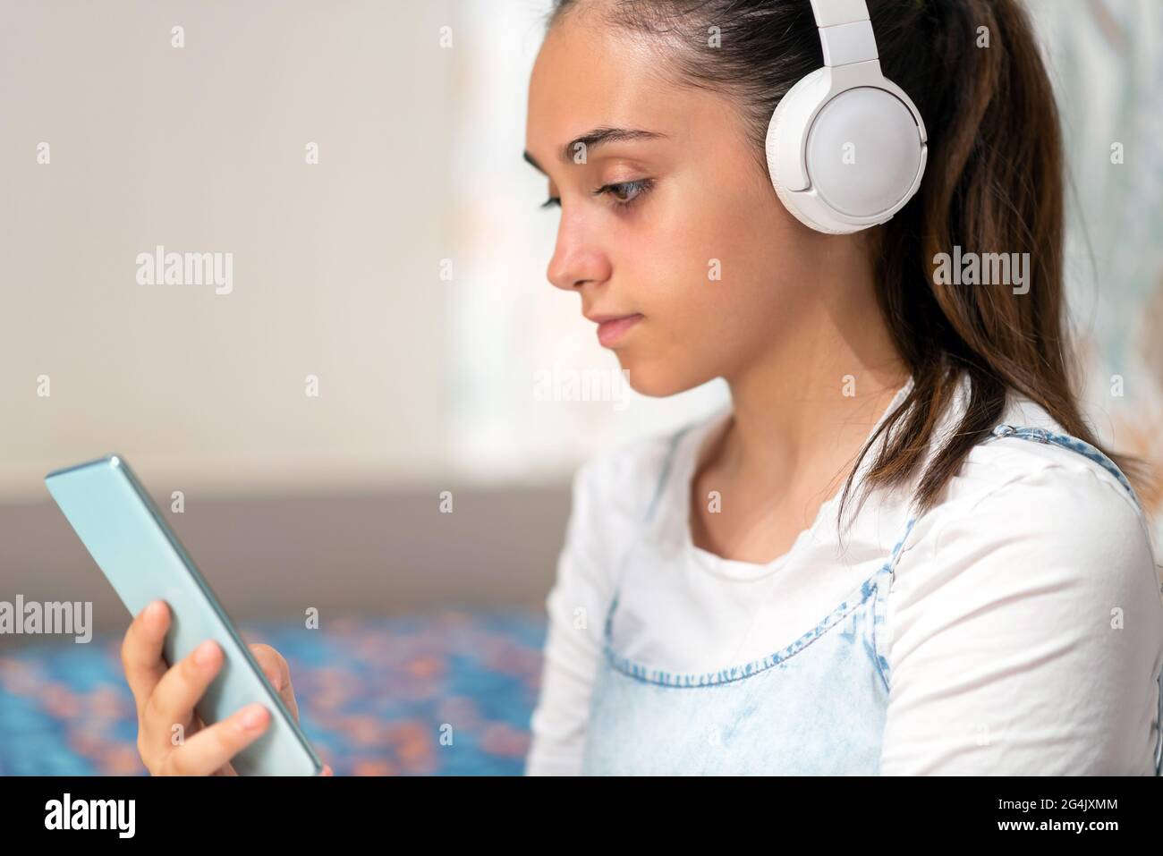 Ha assorbito la giovane ragazza adolescente che ascolta la musica sul suo telefono cellulare utilizzando cuffie stereo all'interno di casa in un ritratto di profilo da vicino ritagliato Foto Stock