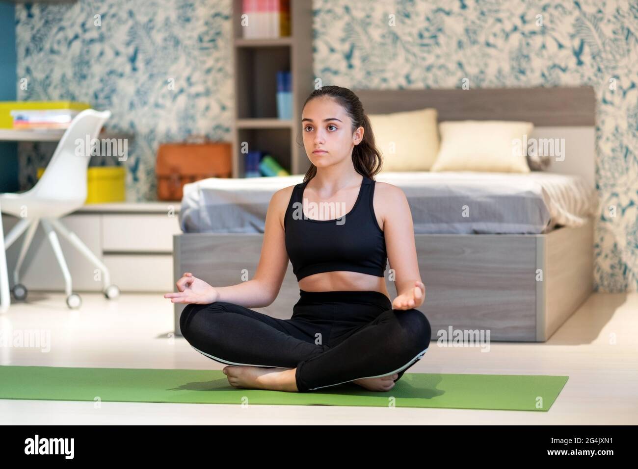 Giovane ragazza teenage seduta rilassante sul pavimento della sua camera da letto meditando mentre facendo la posa yoga lotus in un concetto di benessere, salute e fitness w Foto Stock