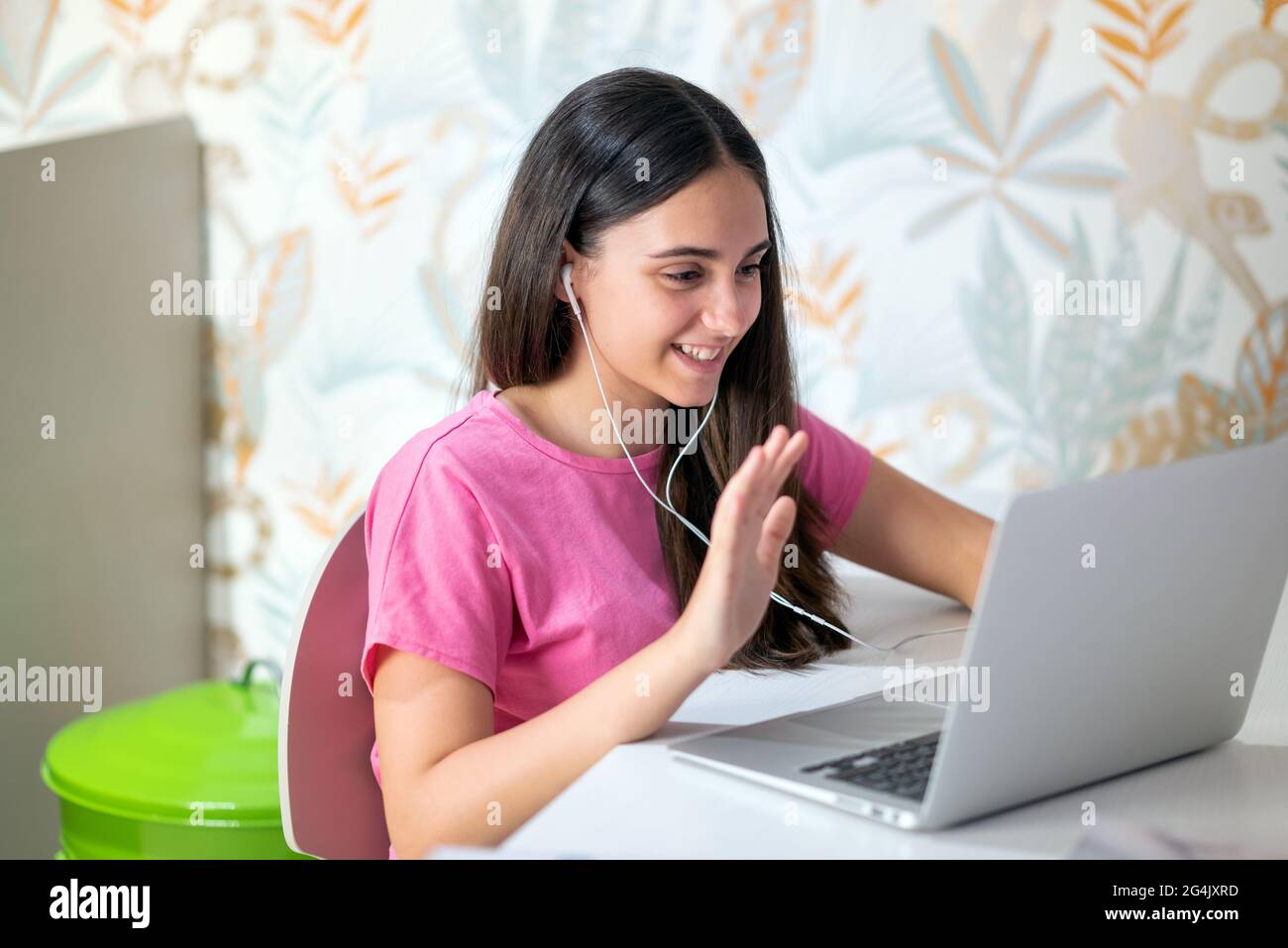 Felice sorridente giovane ragazza adolescente che fa una videoconferenza on-line sul suo computer portatile ondeggiando allo schermo durante il Covid-19 pandemic lockdown o. Foto Stock