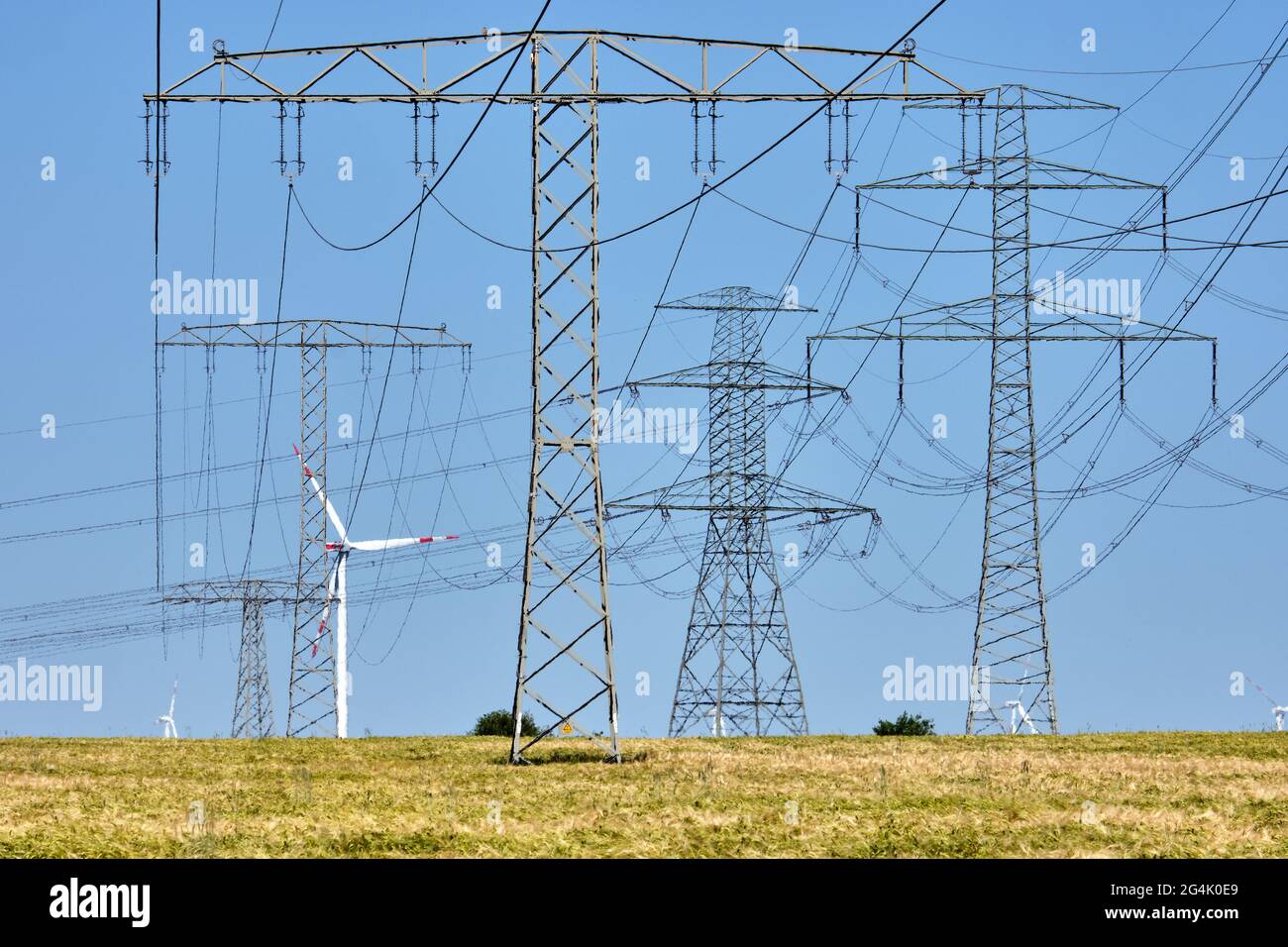 Piloni elettrici e linee elettriche con turbine eoliche sullo sfondo visto in Germania Foto Stock