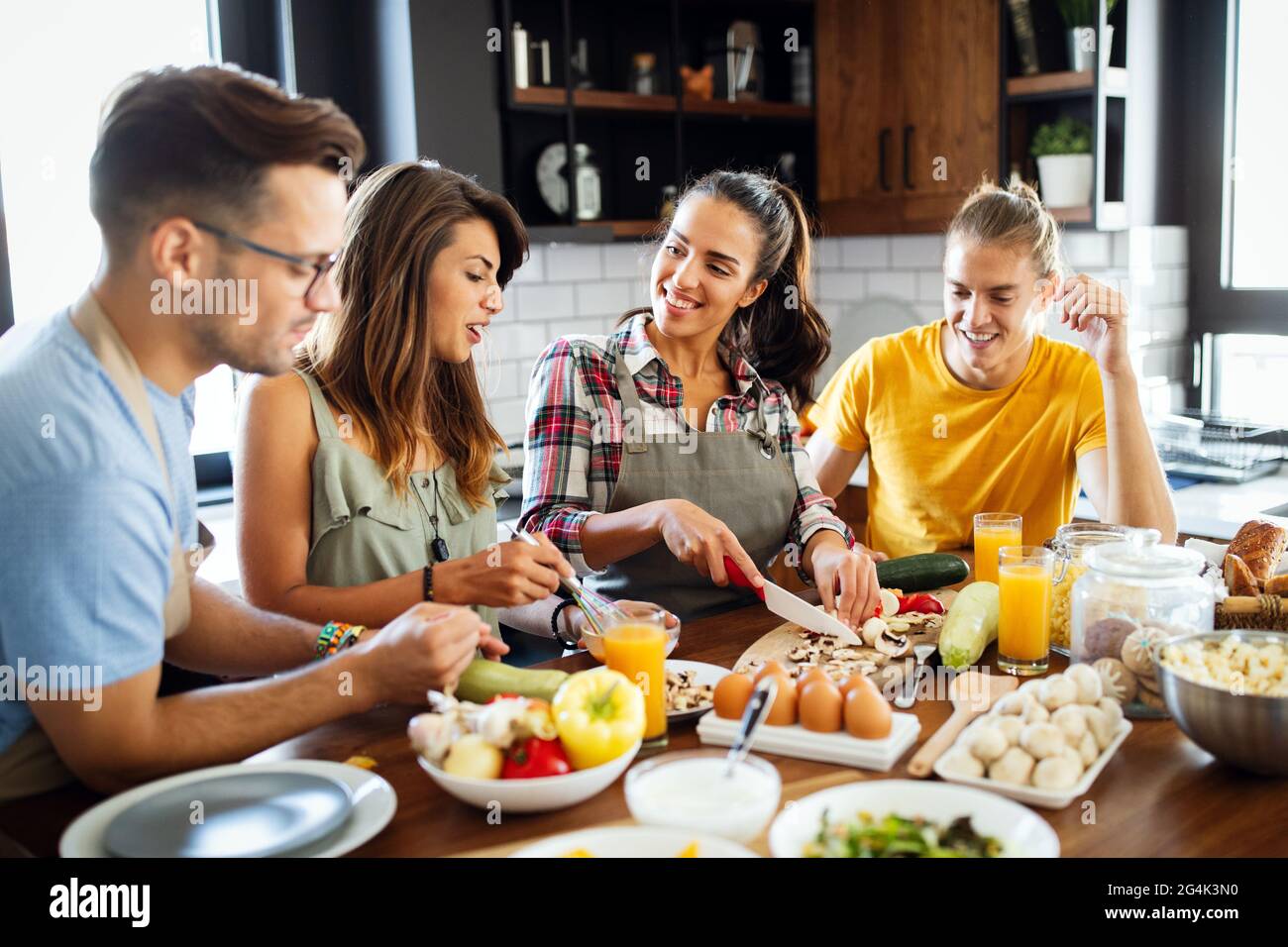 Gruppo di amici felici che ridono e parlano mentre preparano i pasti in cucina Foto Stock