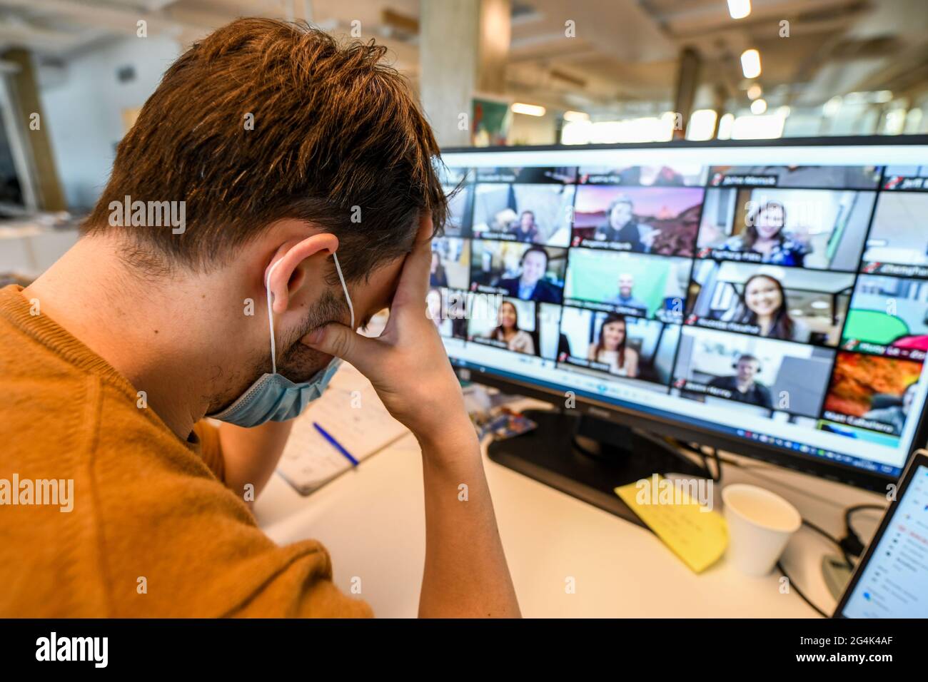 Coronavirus Outbreak, Covid 19, lavoro remoto, videoconferenza in un'azienda. Uomo seduto alla sua scrivania tenendo la testa con le mani Foto Stock