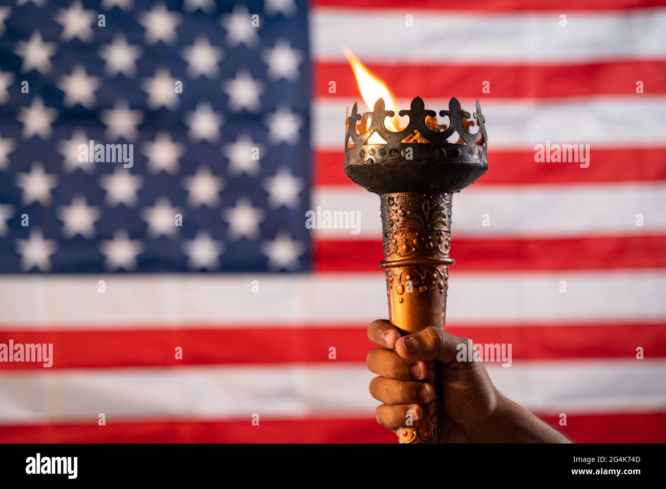 Primo piano di mani che tengono la torcia a fiamma olimpica con bandiera americana o americana come sfondo Foto Stock