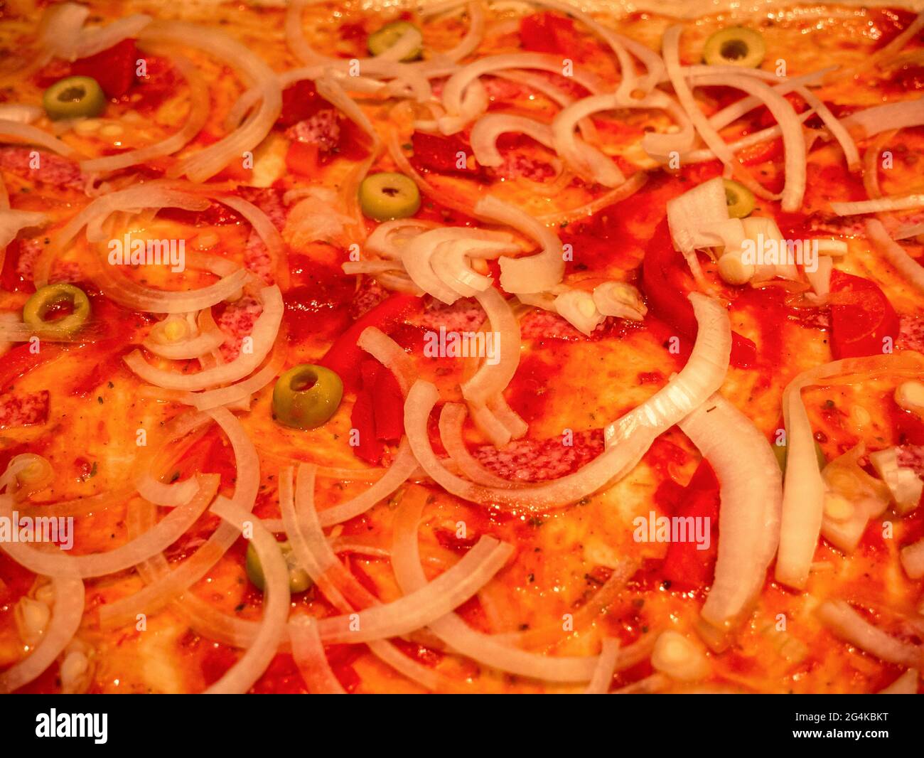Primo piano della pizza cruda prima della cottura, con salsa di pomodoro, cipolla, salame, olive e pepe rosso Foto Stock