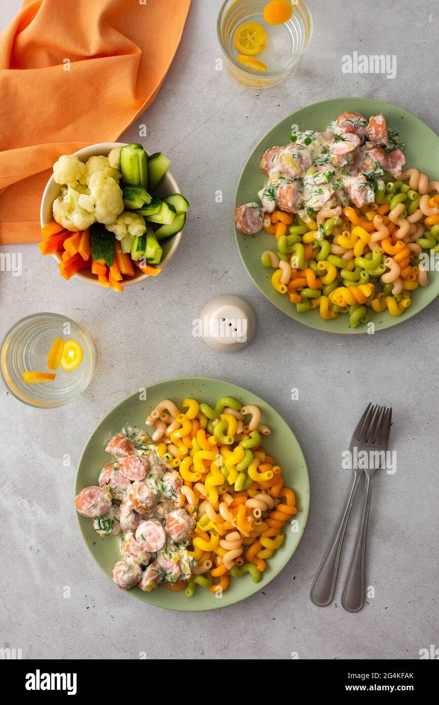 Pasta colorata con salsicce bollite in salsa di panna acida, verdure fresche e cavolfiore bollito, acqua con kumquat Foto Stock