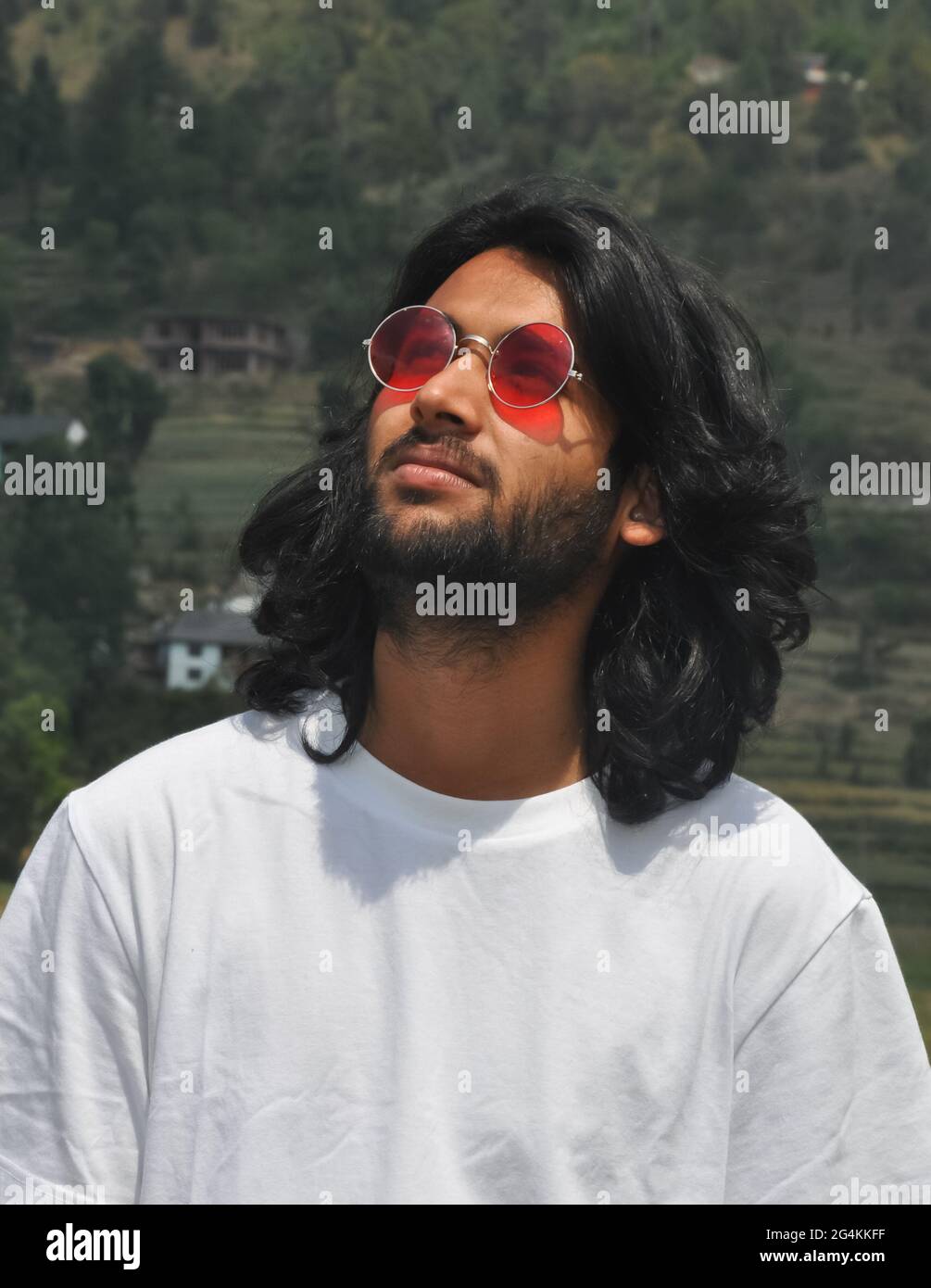 Ritratto di un bell'aspetto lungo capelli indiani giovani uomini indossando occhiali da sole con guardare in su, UN bel ragazzo bearded in piedi fuori con indossare t-shirt bianca Foto Stock