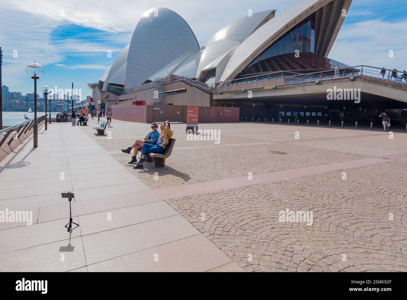 Due giovani donne si siedono su un posto fuori dalla Sydney Opera House nel nuovo Galles del Sud, Australia e scattano una foto selfie con un telefono su un treppiede Foto Stock