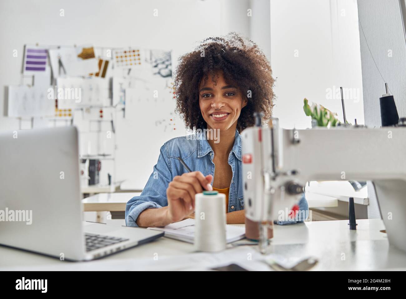 Sorridente afroamericana con computer portatile si siede sul posto di lavoro in studio Foto Stock