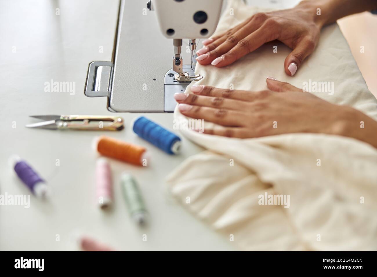 Seamstress afroamericano cucce tessuto bianco con macchina sul posto di lavoro in studio Foto Stock