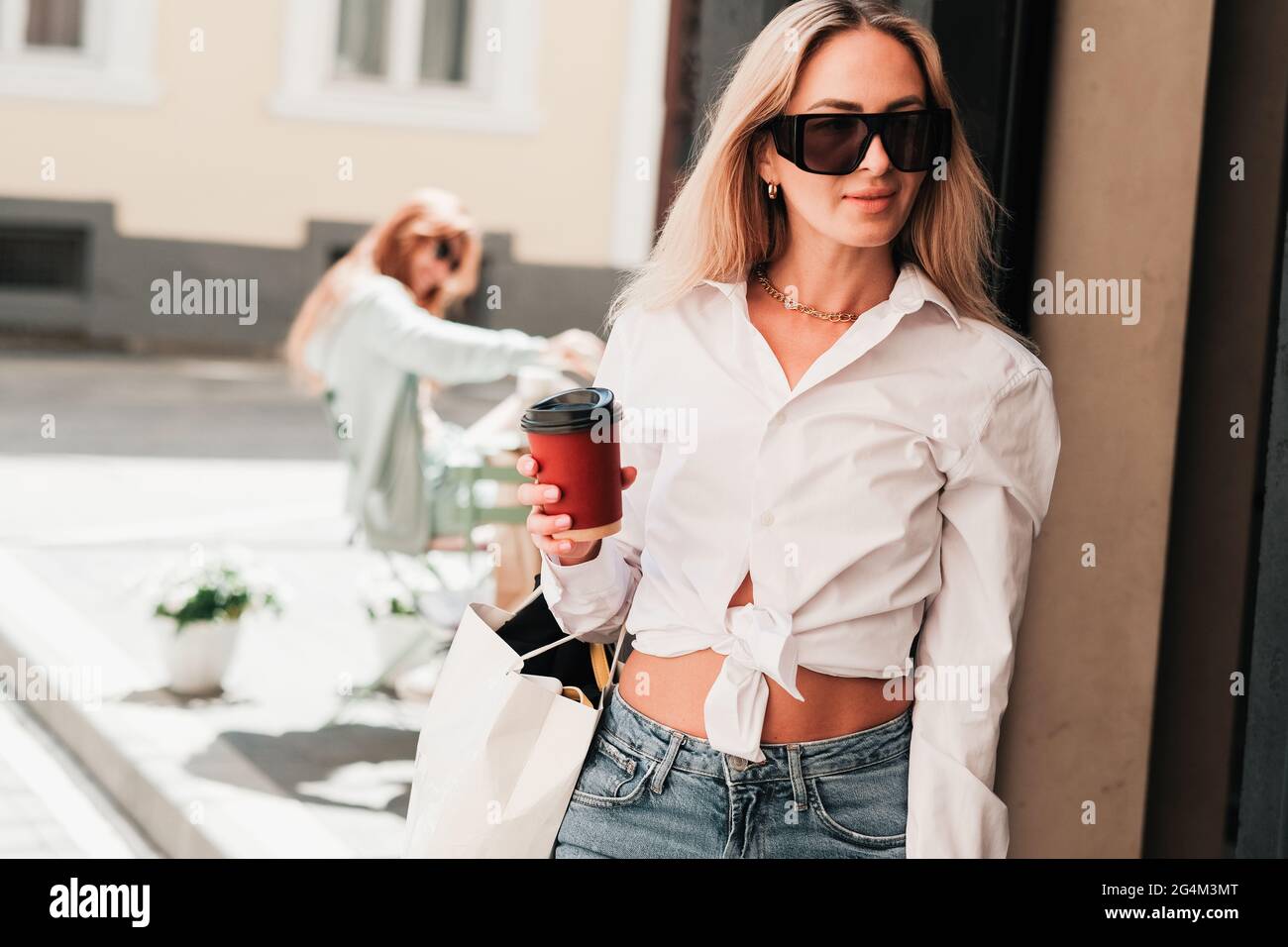 Donna elegante che esce da un caffè, tenendo in mano una tazza di caffè e guardando via, imprenditore donna fiducioso che indossa occhiali da sole, Coffee To Go Foto Stock