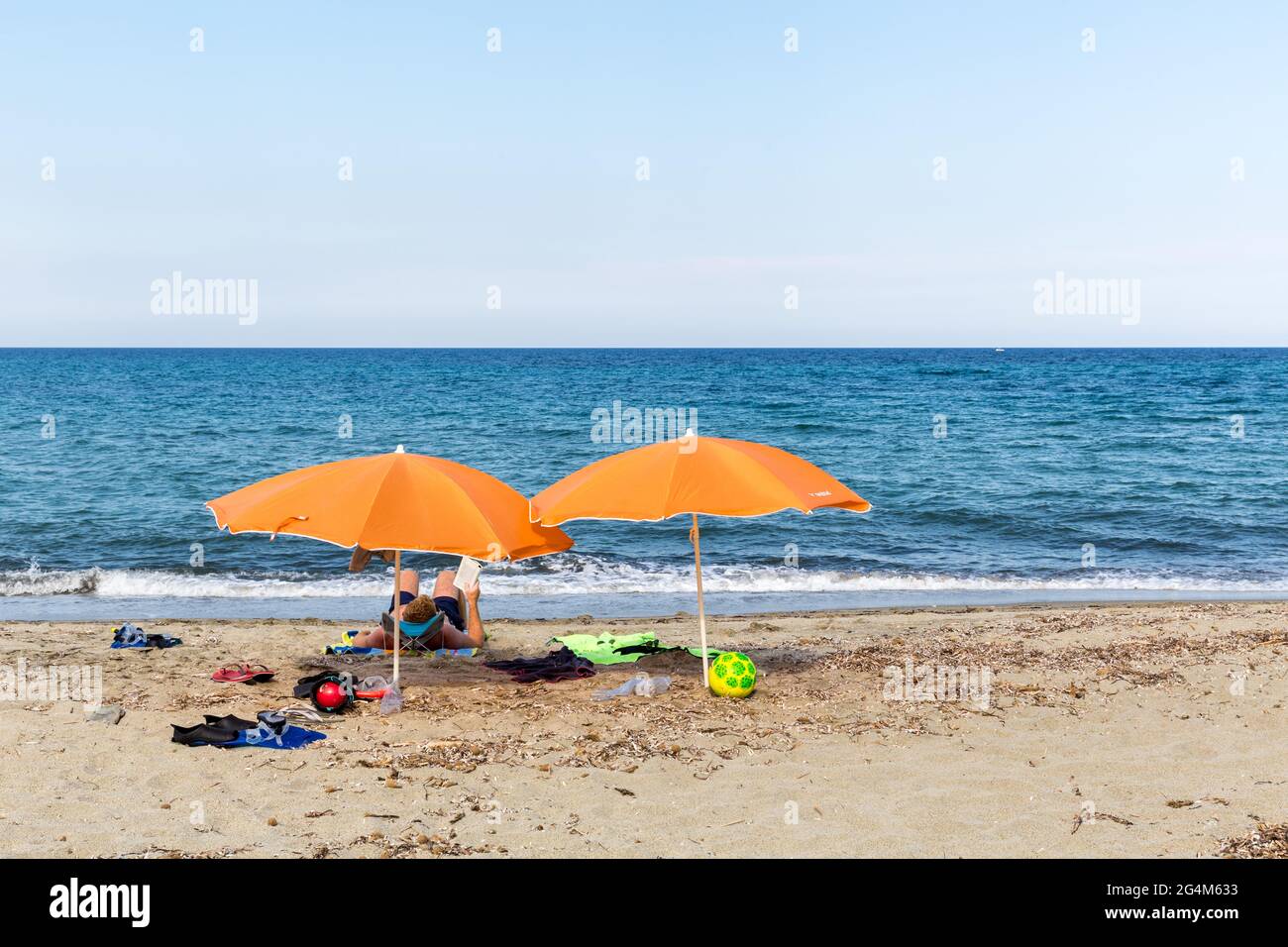 Persona che riposa sotto due ombrelli arancioni sulla spiaggia di Prunete. Corsica, Francia Foto Stock