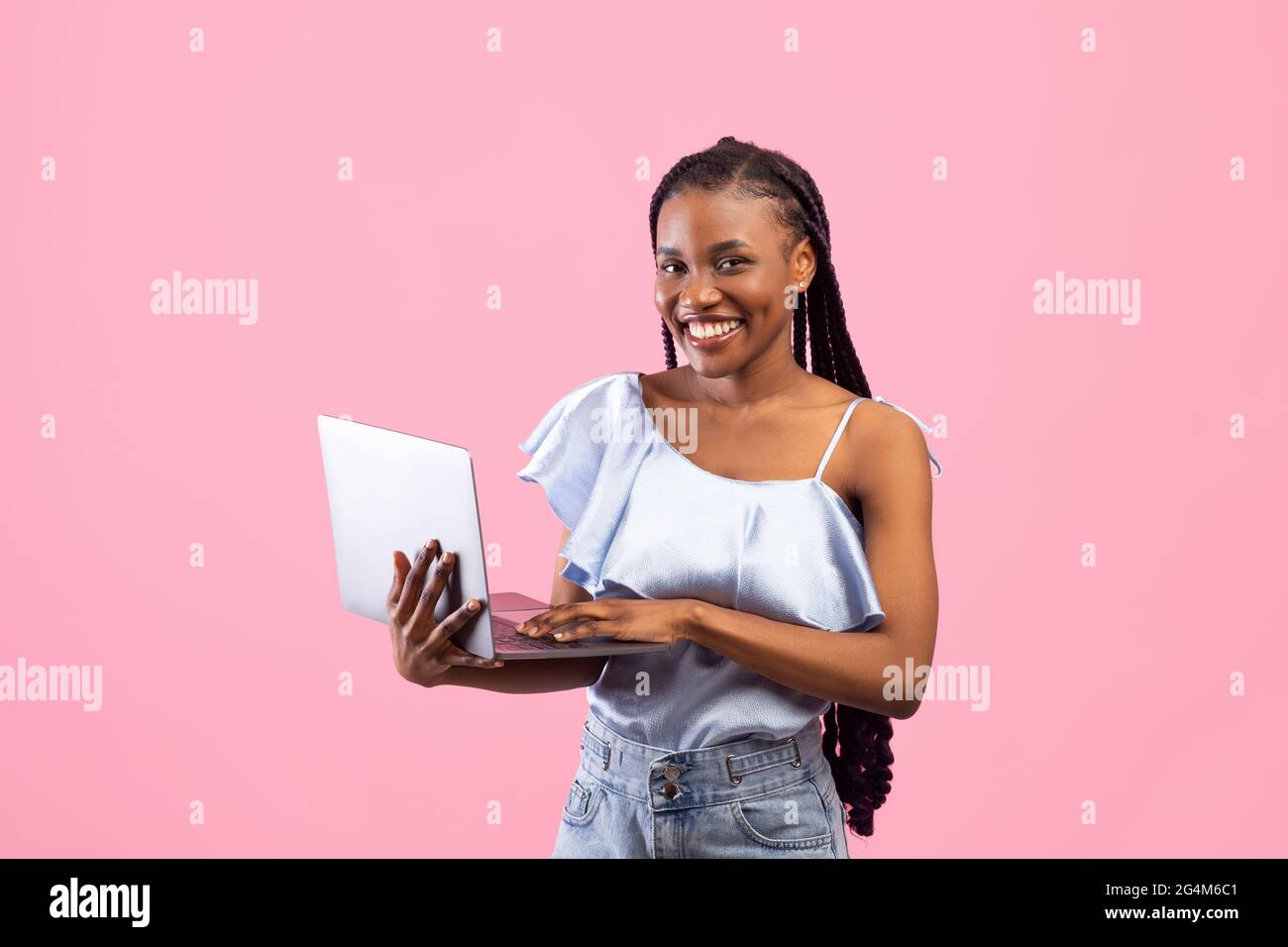 Giovane donna afroamericana con grappoli afro che usano computer portatile, lavorando o studiando online su sfondo rosa Foto Stock