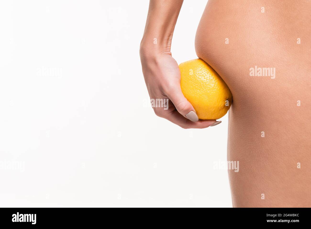 primo piano vista della giovane donna che fa massaggio anticellulite di natiche con arancio in mano isolato su bianco Foto Stock