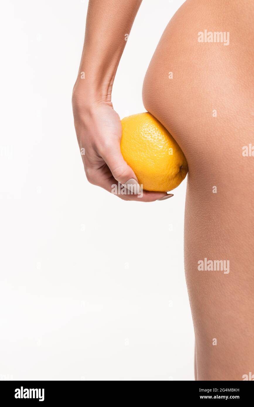 primo piano vista della giovane donna che fa massaggio anticellulite di natiche con arancio isolato su bianco Foto Stock