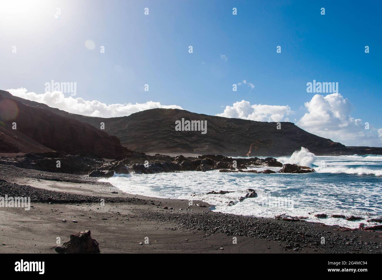 Canarie, Lanzarote, costa con tipica spiaggia nera e forte surf. Sullo sfondo il tipico paesaggio vulcanico Foto Stock