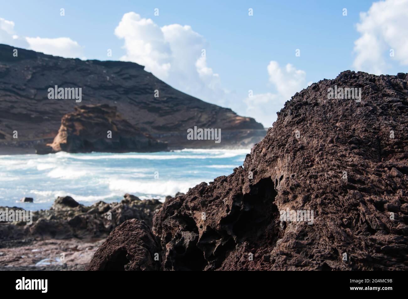 Isole Canarie, Lanzarote. Costa con tipiche rocce laviche nere e fredde e forte surf. Sullo sfondo il tipico paesaggio vulcanico Foto Stock