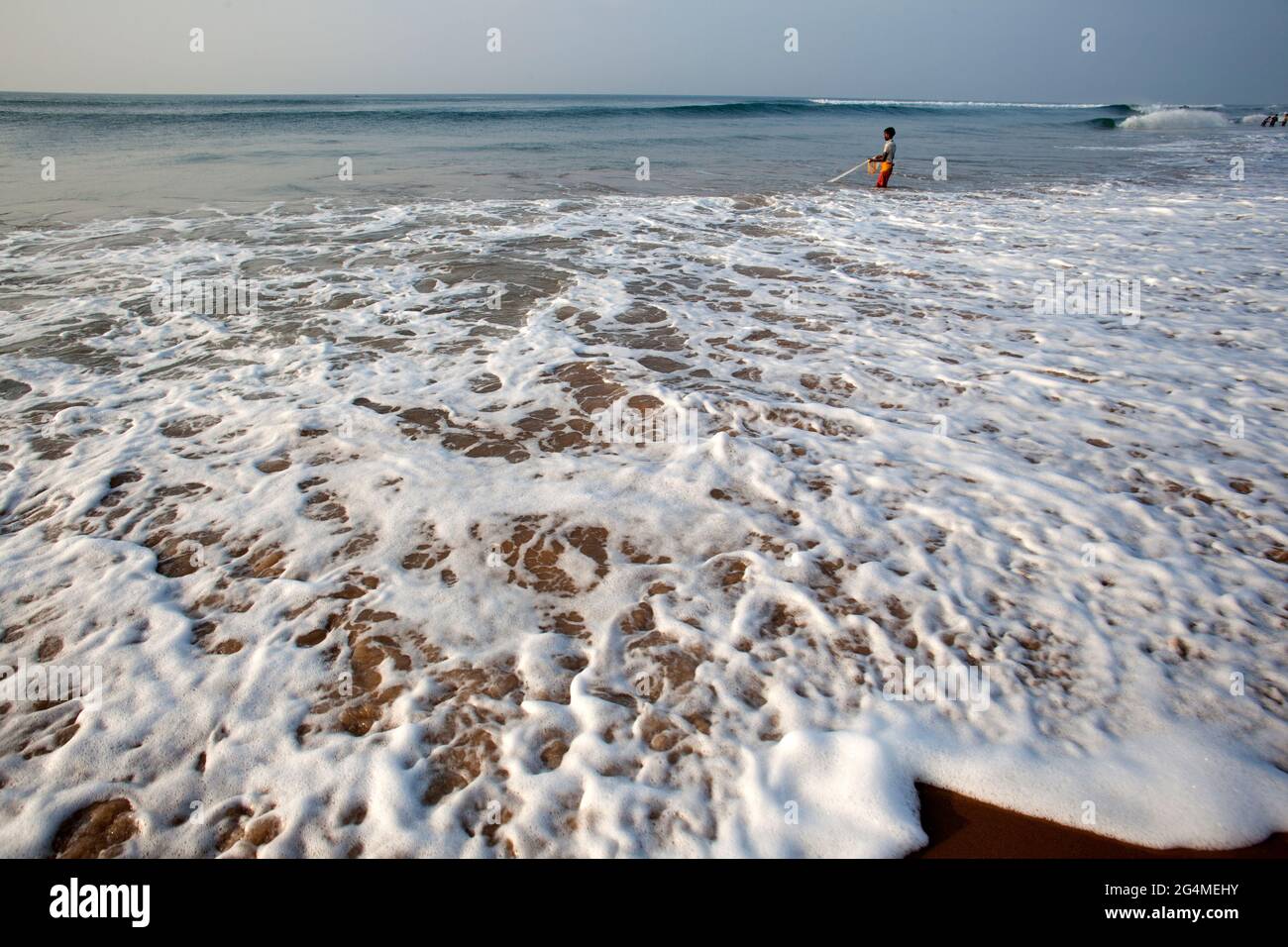 Un pescatore che cerca di catturare il pesce gettando la rete nel mare ondulato a Puri, una famosa spiaggia marina turistica dell'India orientale. Foto Stock