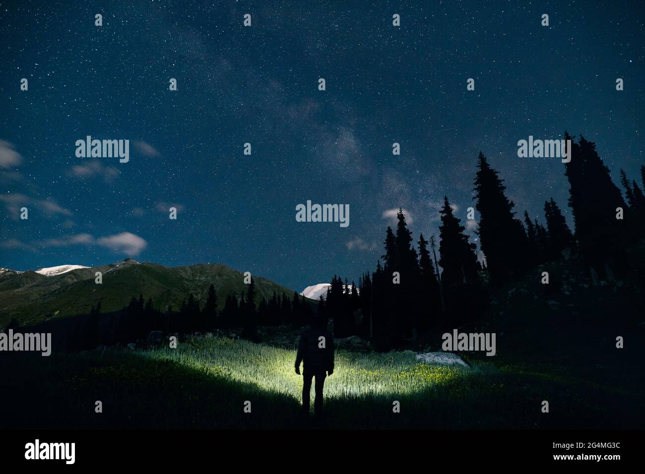 La silhouette dell'uomo illumina il campo con faro in montagna sotto il cielo notturno con stelle. Foto Stock
