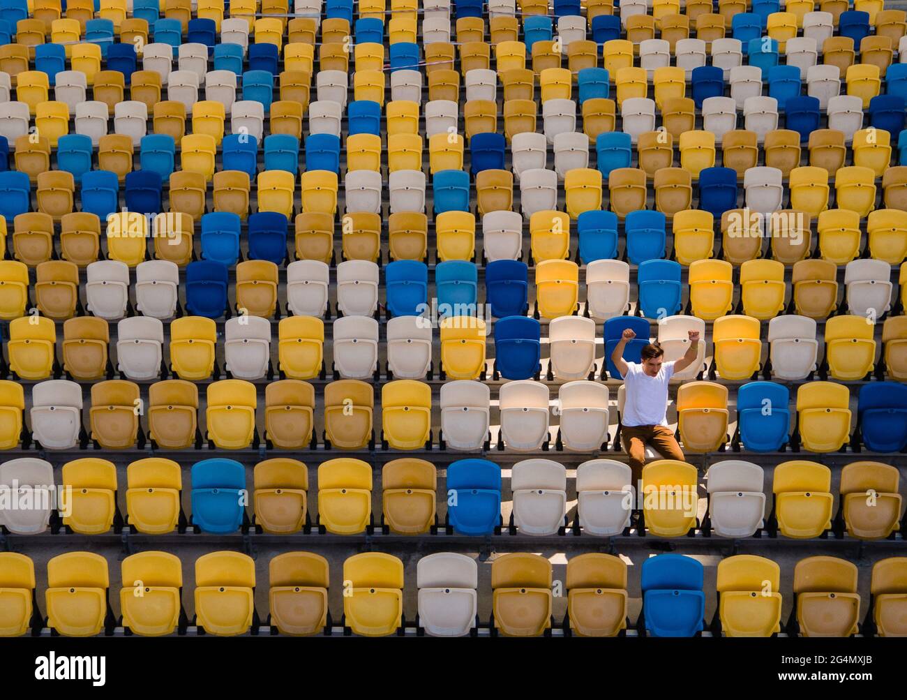 Un ragazzo in una t-shirt bianca sta cantando su una tribuna vuota di uno stadio di calcio Foto Stock
