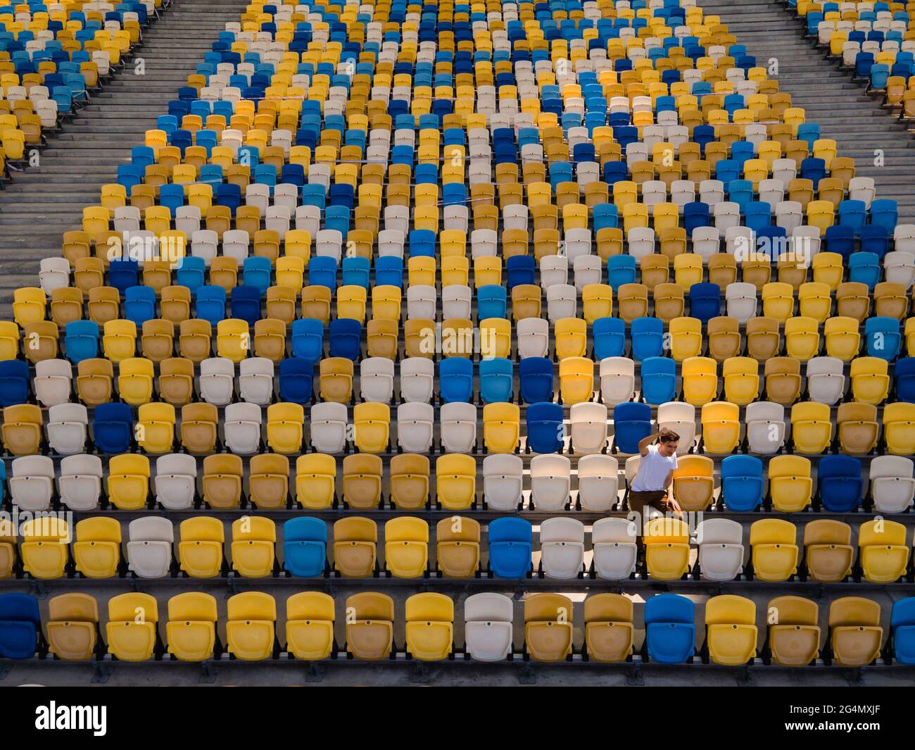 Un ragazzo in una t-shirt bianca sta cantando su una tribuna vuota di uno stadio di calcio Foto Stock