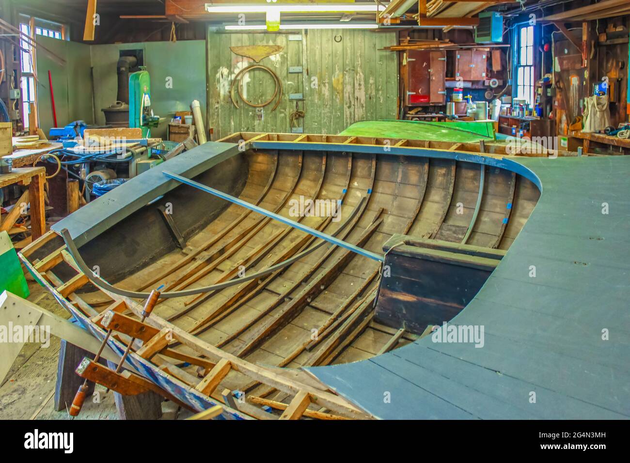 Imbarcazione in legno parzialmente costruita in un vecchio laboratorio di marina scuro con luci fluorescenti - fuoco selettivo e luminoso riflesso luminoso nelle finestre Foto Stock