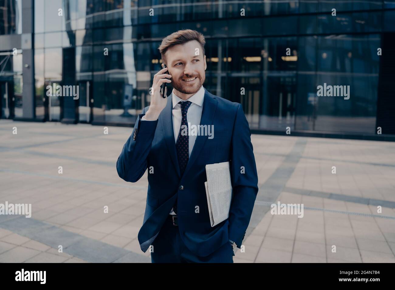 Buon lavoratore d'ufficio con giornali che parlano sullo smartphone Foto Stock