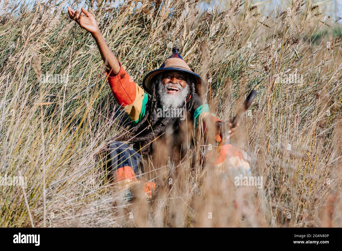 Allegro rastafari etnici con dreadlock guardando la telecamera in piedi in un prato asciutto nella natura Foto Stock