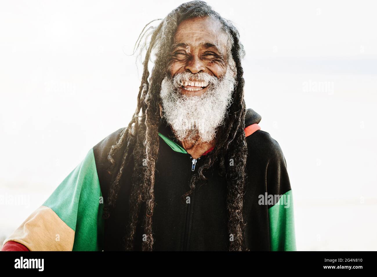 Ritratto di allegro rastafari etnico con dreadlock guardando la fotocamera nella natura con sfondo bianco Foto Stock