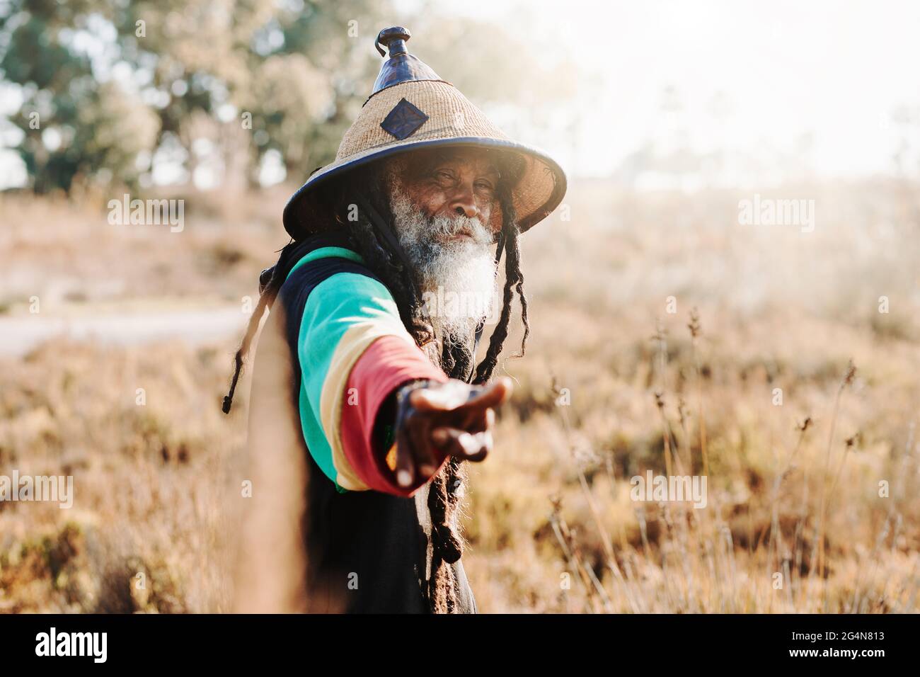 Allegro rastafari etnici con dreadlock guardando la telecamera in piedi in un prato asciutto nella natura Foto Stock