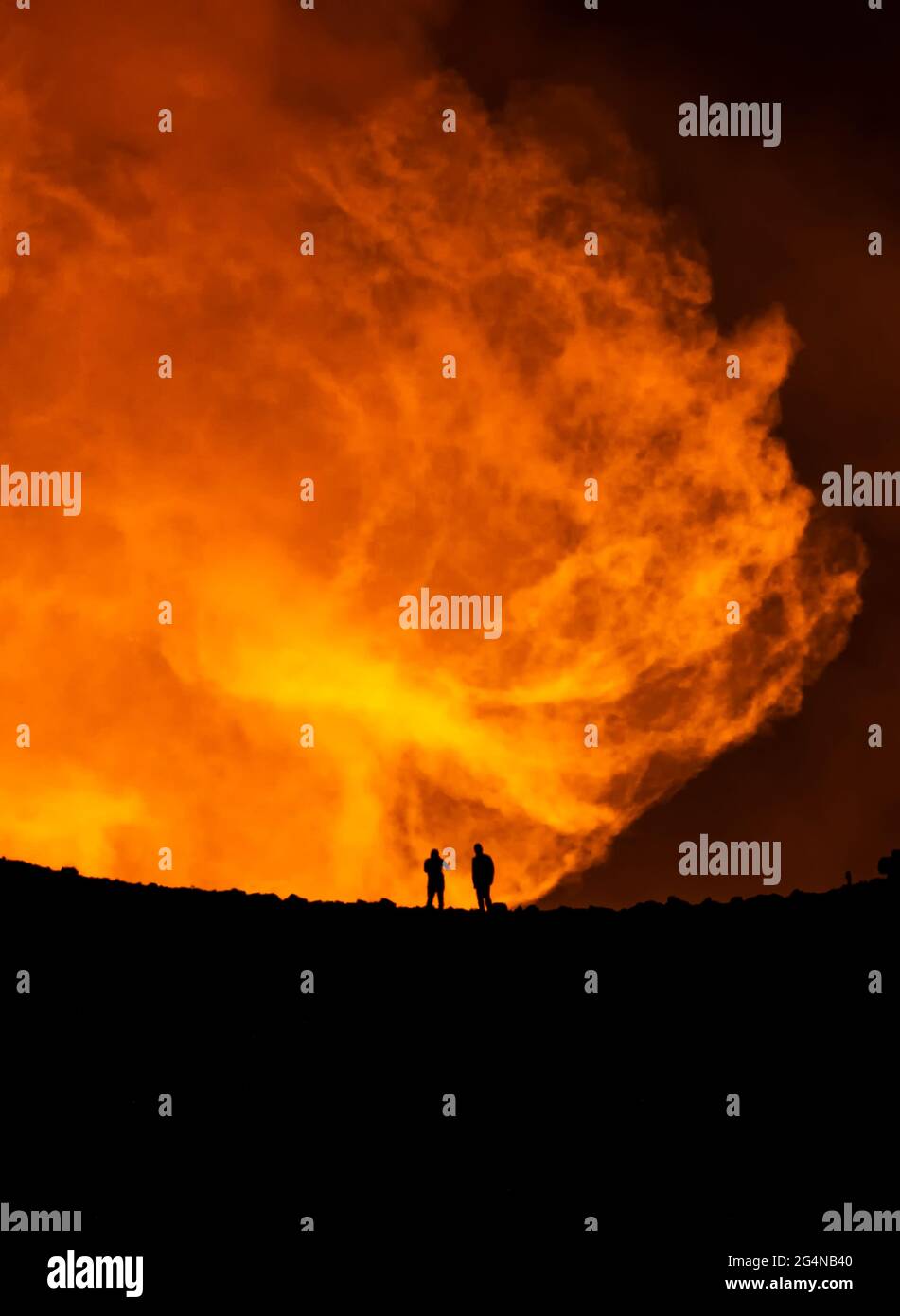 Silhouette di viaggiatori anonimi che si levano contro il profumo arancione del vulcano attivo in Islanda Foto Stock