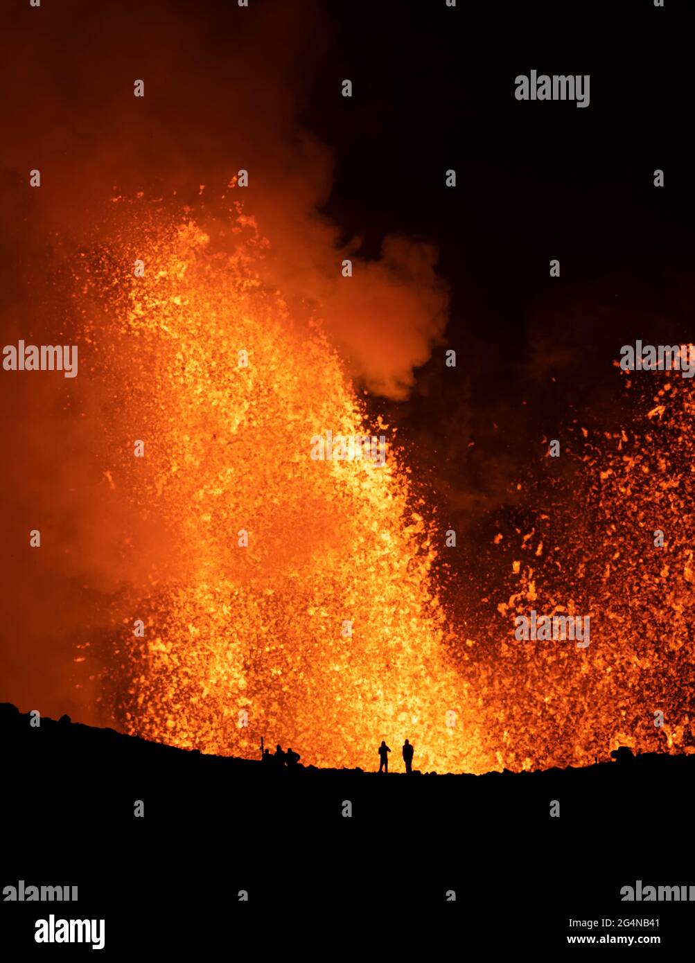 Silhouette di viaggiatori anonimi che si levano contro il profumo arancione del vulcano attivo in Islanda Foto Stock