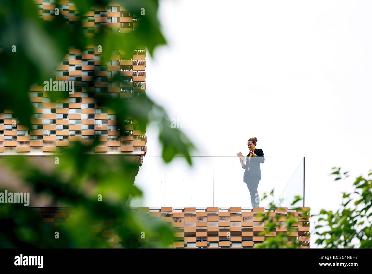 Da sotto di donna in abito elegante in piedi sul balcone di un edificio moderno con elementi geometrici sulle finestre mentre si usa un tablet vicino a ringhiera di vetro Foto Stock