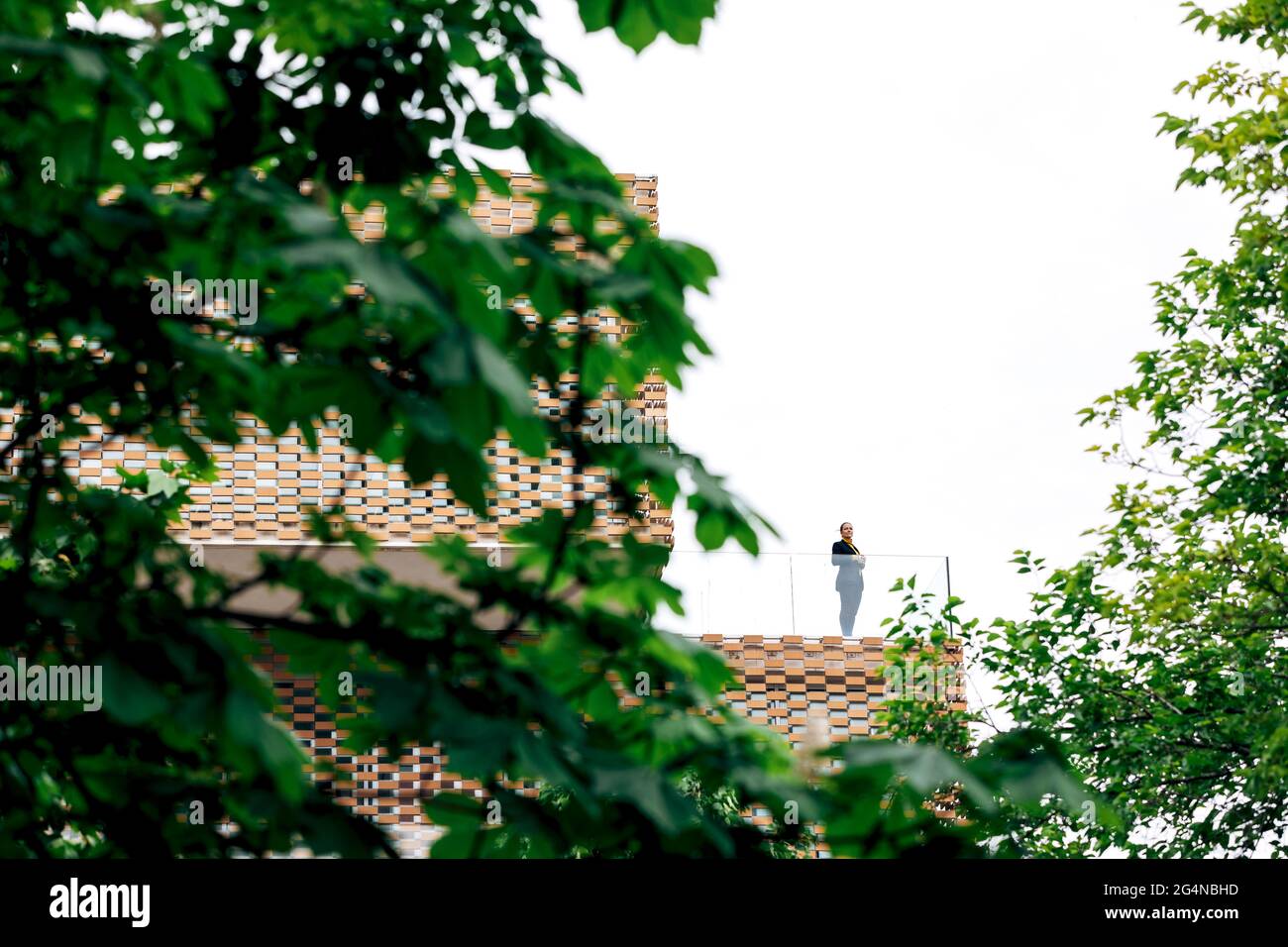Da sotto di donna in abito elegante in piedi sul balcone di un edificio moderno con elementi geometrici sulle finestre mentre si usa un tablet vicino a ringhiera di vetro Foto Stock