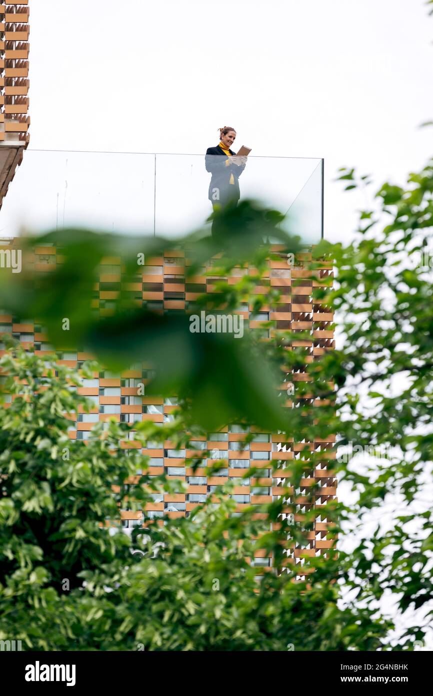 Da sotto di donna in abito elegante in piedi sul balcone di un edificio moderno con elementi geometrici sulle finestre mentre si usa un tablet vicino a ringhiera di vetro Foto Stock
