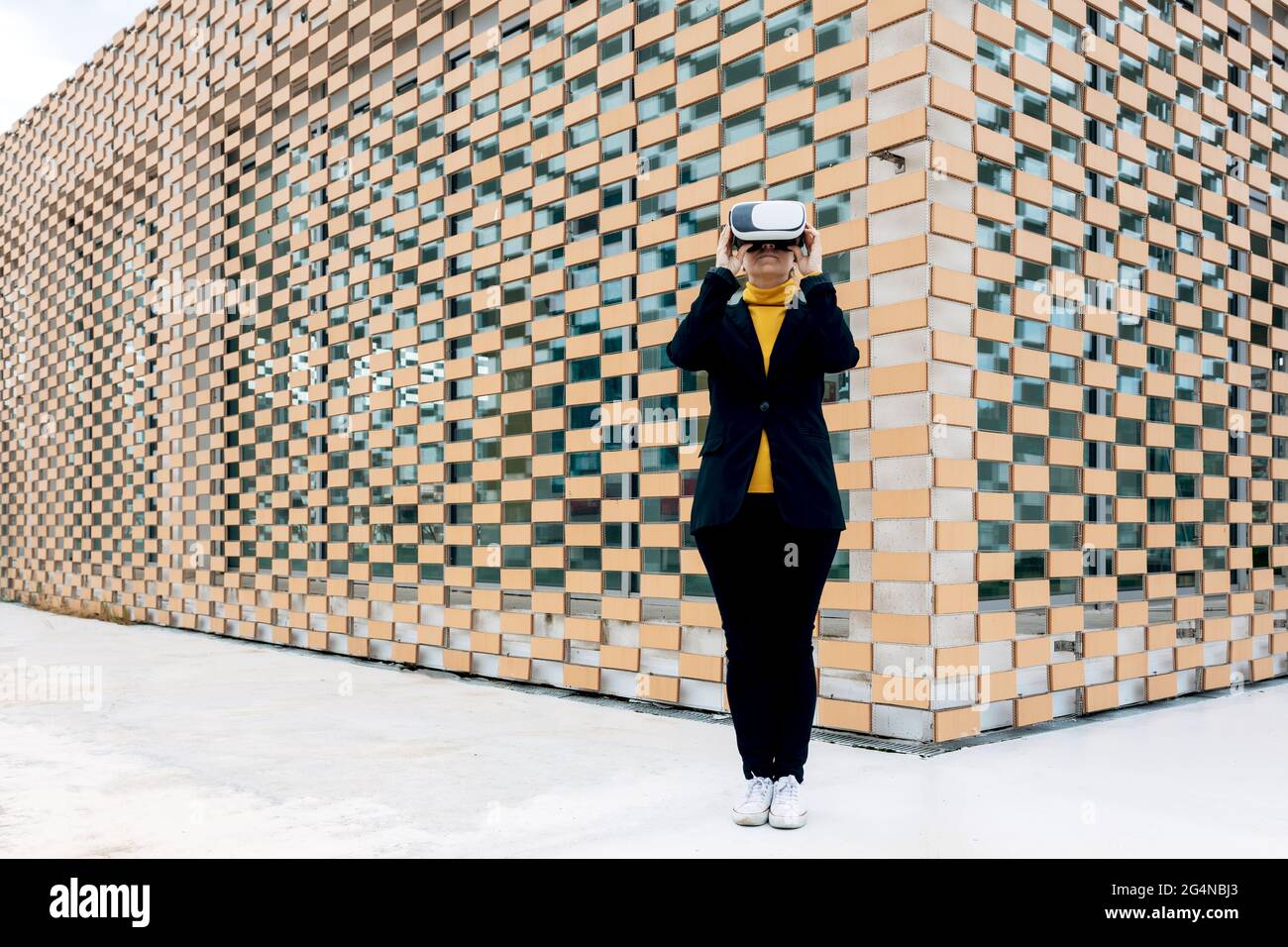 Donna in giacca e dolcevita con occhiali VR vicino alle finestre dell'edificio nella luce del giorno Foto Stock
