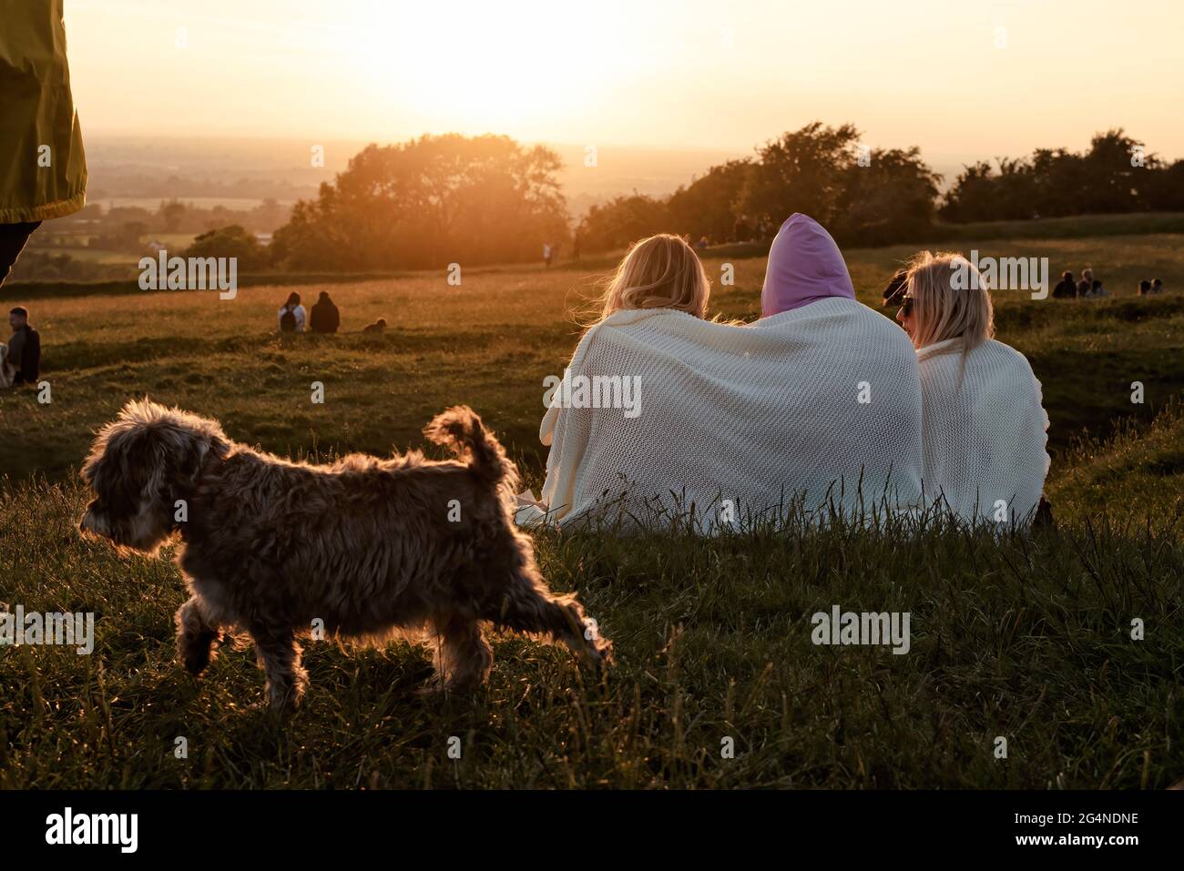 Contea di Meath, Irlanda. 21 Giugno 2021. Tre donne che si siedono e guardano il tramonto mentre un piccolo cane cammina by.centinaia di persone si sono riunite nella collina di Tara ieri sera per il Solstizio d'Estate del 2021. Ogni anno, la gente si riunisce sulla collina di Tara per celebrare il solstizio estivo, che è stato un luogo spirituale e storico per migliaia di anni. Credit: SOPA Images Limited/Alamy Live News Foto Stock